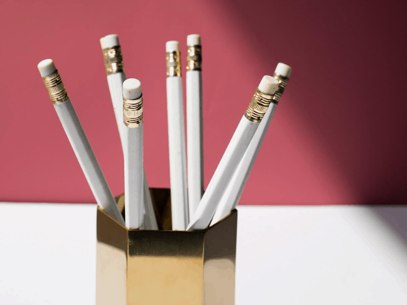white pencils with eraser and gold trim, upside down pencils in gold six sided pencil pot holder, white desk, red background, working from home essentials, social squares image, 